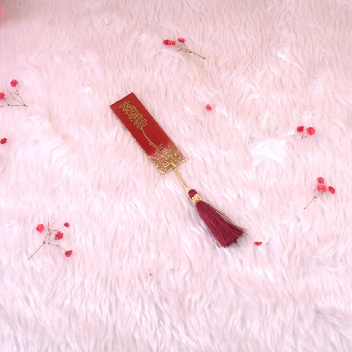 Decorative red and gold bookmark with tassel on a pink textured background