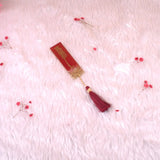 Decorative red and gold bookmark with tassel on a pink textured background
