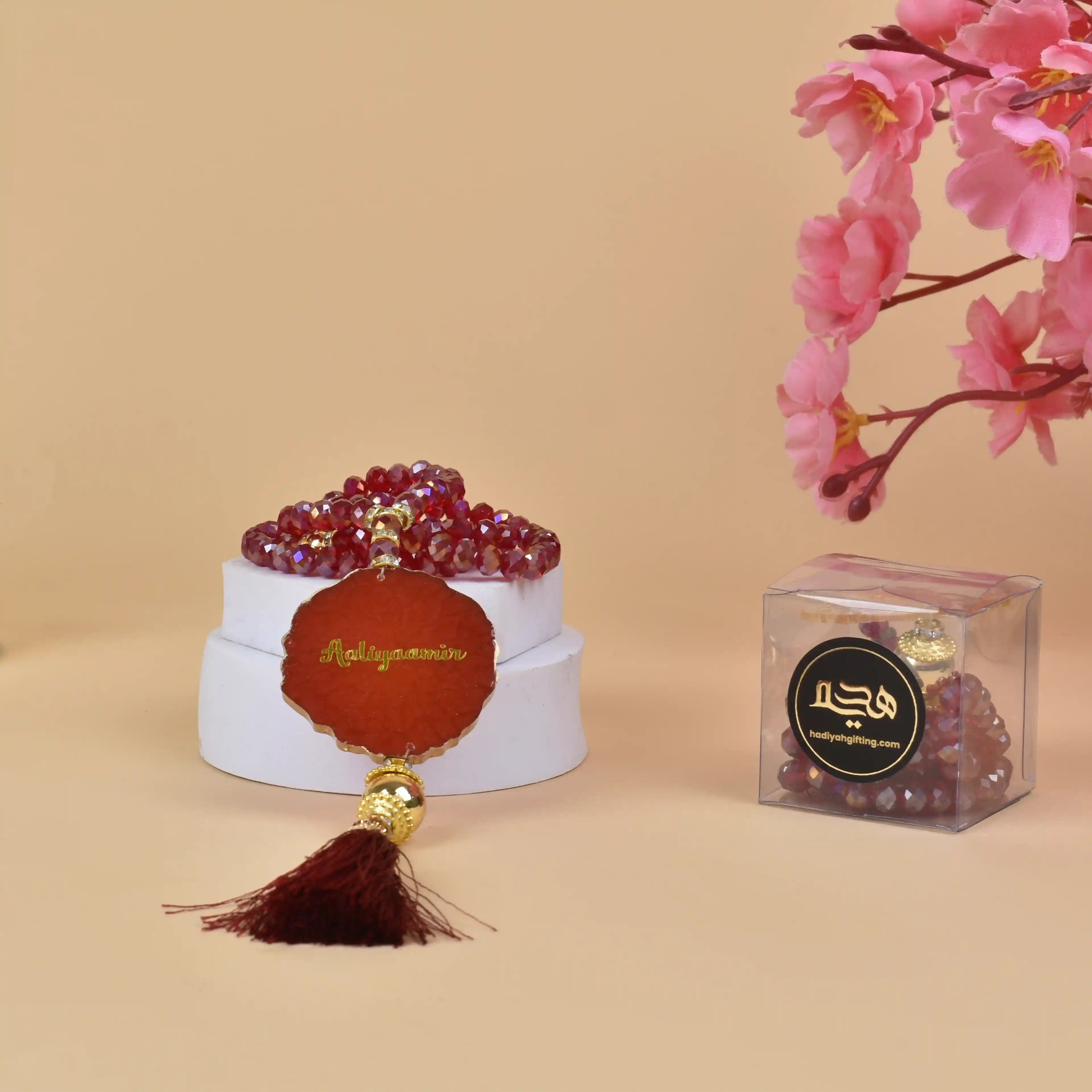 Red crystal tasbeeh with engraved name 'Abdulquddus' in gold, paired with a dark red tassel. Unique custom Islamic gift for ceremonies. Main image