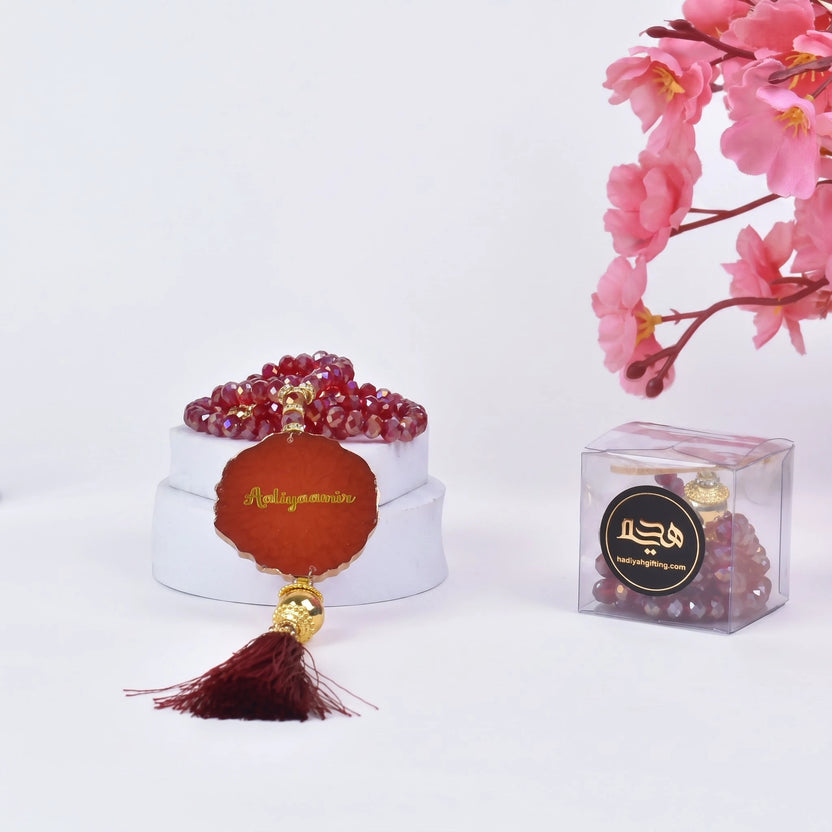 Red crystal tasbeeh with engraved name 'Abdulquddus' in gold, paired with a dark red tassel. Unique custom Islamic gift for ceremonies. Main image