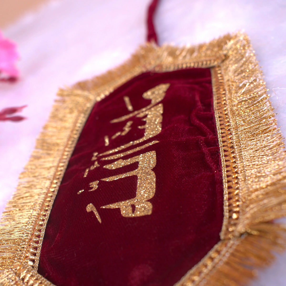 Close-up of elegant Mashallah Band featuring gold Arabic script and fringe on maroon velvet, perfect for wedding decor and Islamic blessings.