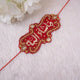 Decorative red and gold rakhi on a white background with white flowers.