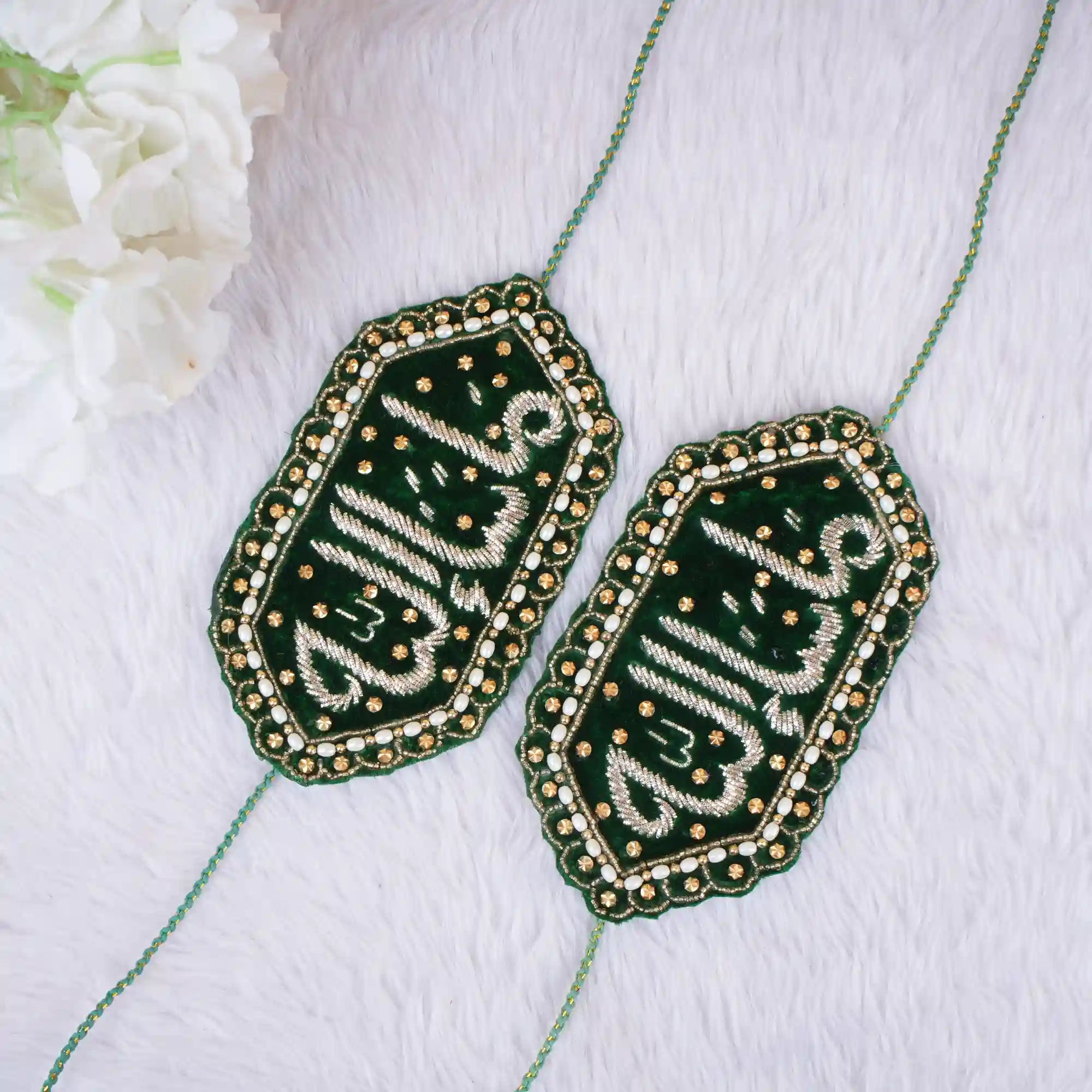 Two green embroidered patches with gold detailing on a white fabric background.