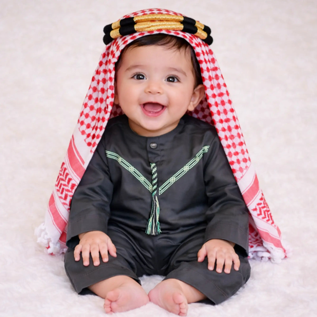 Baby boy in traditional red and white keffiyeh with black thobe on white fluffy background