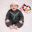 Baby boy in traditional black attire with white embroidery, lying on white plush surface