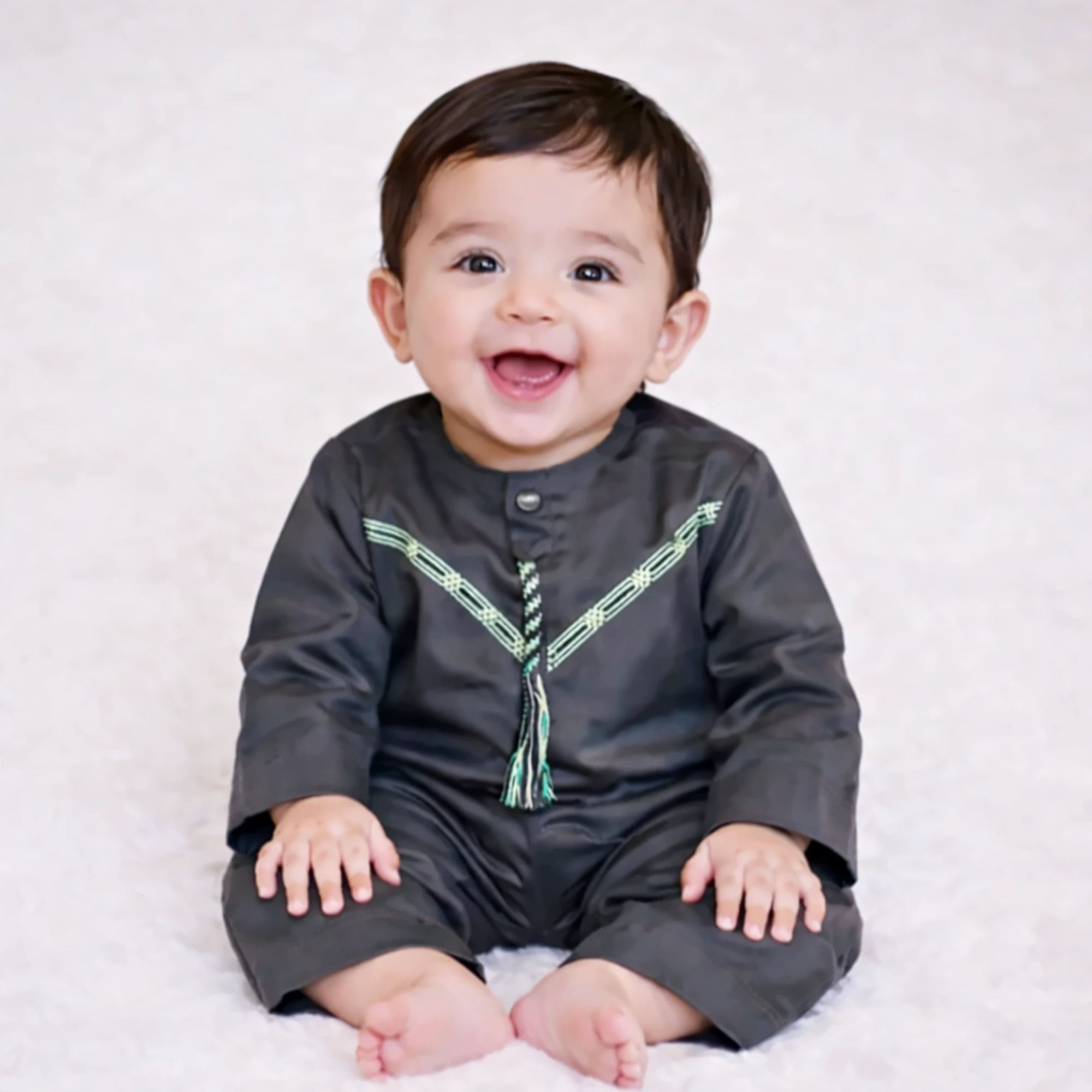 Baby boy smiling in black traditional outfit on white background Main image