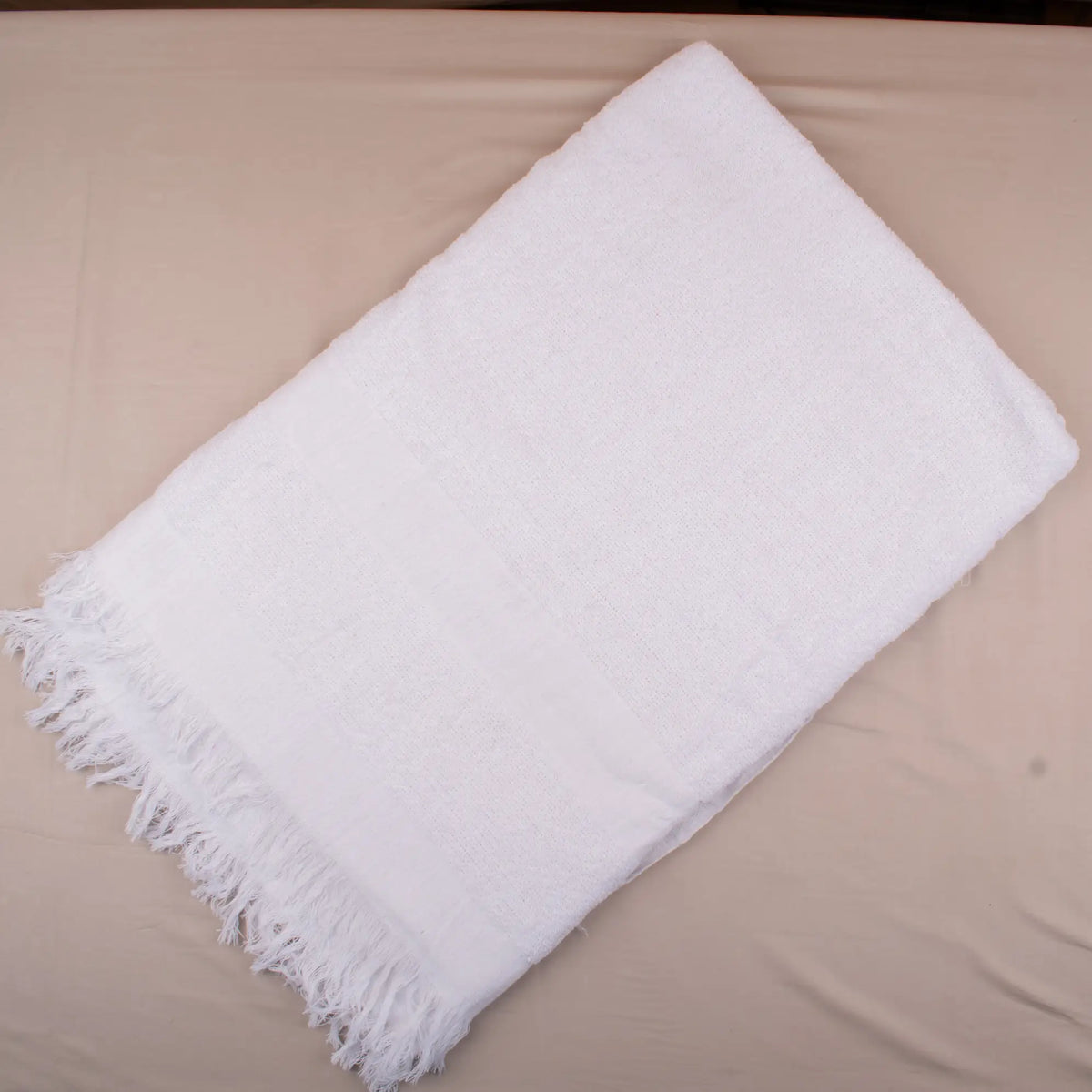 White towel with fringes on a beige surface