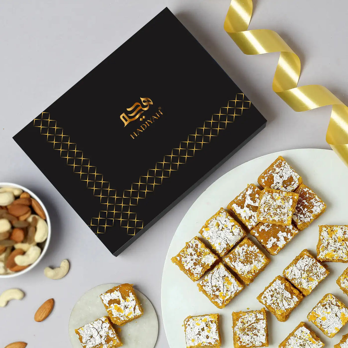 Premium Moong Dal Barfi with Desi Ghee topped with silver leaf, served on a plate beside a luxury gift box, perfect for weddings and Eid gifts.