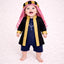 Baby boy in traditional black and gold Islamic outfit with red and white keffiyeh, standing on white textured background