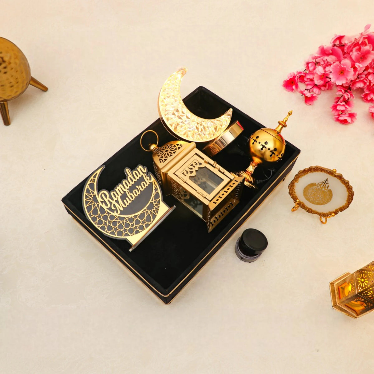 Flat lay of Nazakat Luxury Ramadan Hamper with Islamic decor and moon lamp in a velvet tray, surrounded by festive pink flowers for Ramadan gifting.