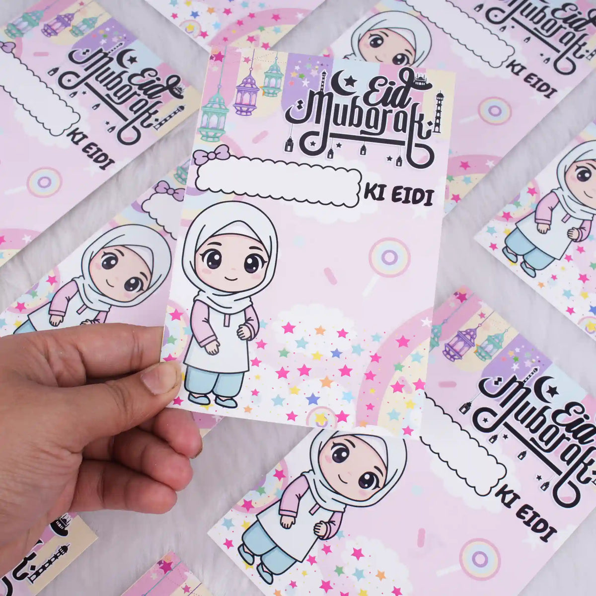 A hand holding a pink premium Eidi card for girls, showing a cute cartoon girl illustration and space to write a name.