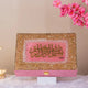 Decorative box with gold and pink design on a white surface with pink flowers in the background