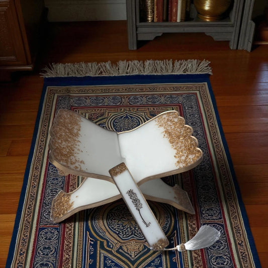 Foldable offwhite resin Quran stand with gold detailing and matching bookmark placed on a prayer mat, perfect for Hajj & Umrah gifts.