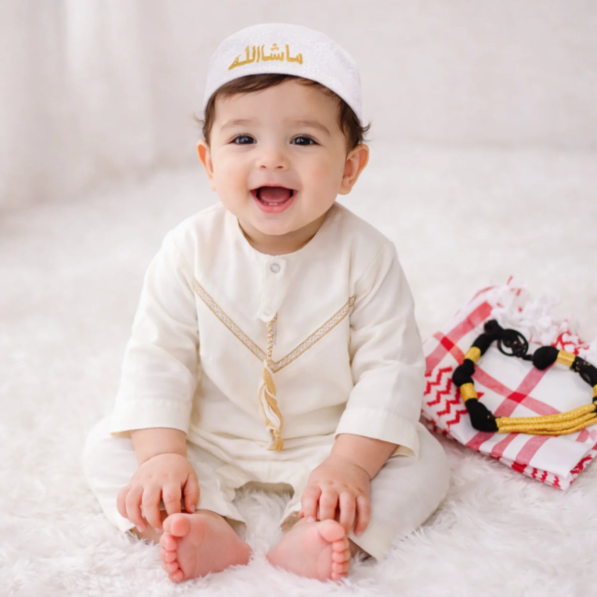 Baby boy with traditional white thobe and red checkered headscarf smiling