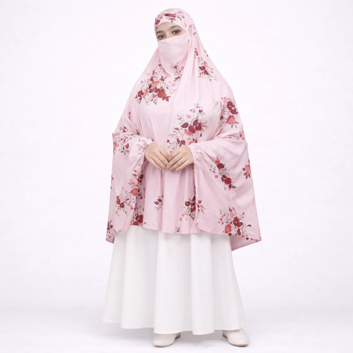 Woman modeling a light pink floral printed prayer makhana (prayer dress) with an attached face veil, paired with a white skirt against a white background.
