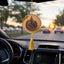 Decorative hanging car ornament with tassel inside a car, blurred street view outside.