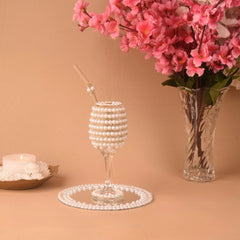 Decorative glass with pearl-like beads, a vase of pink flowers, and a candle on a beige background