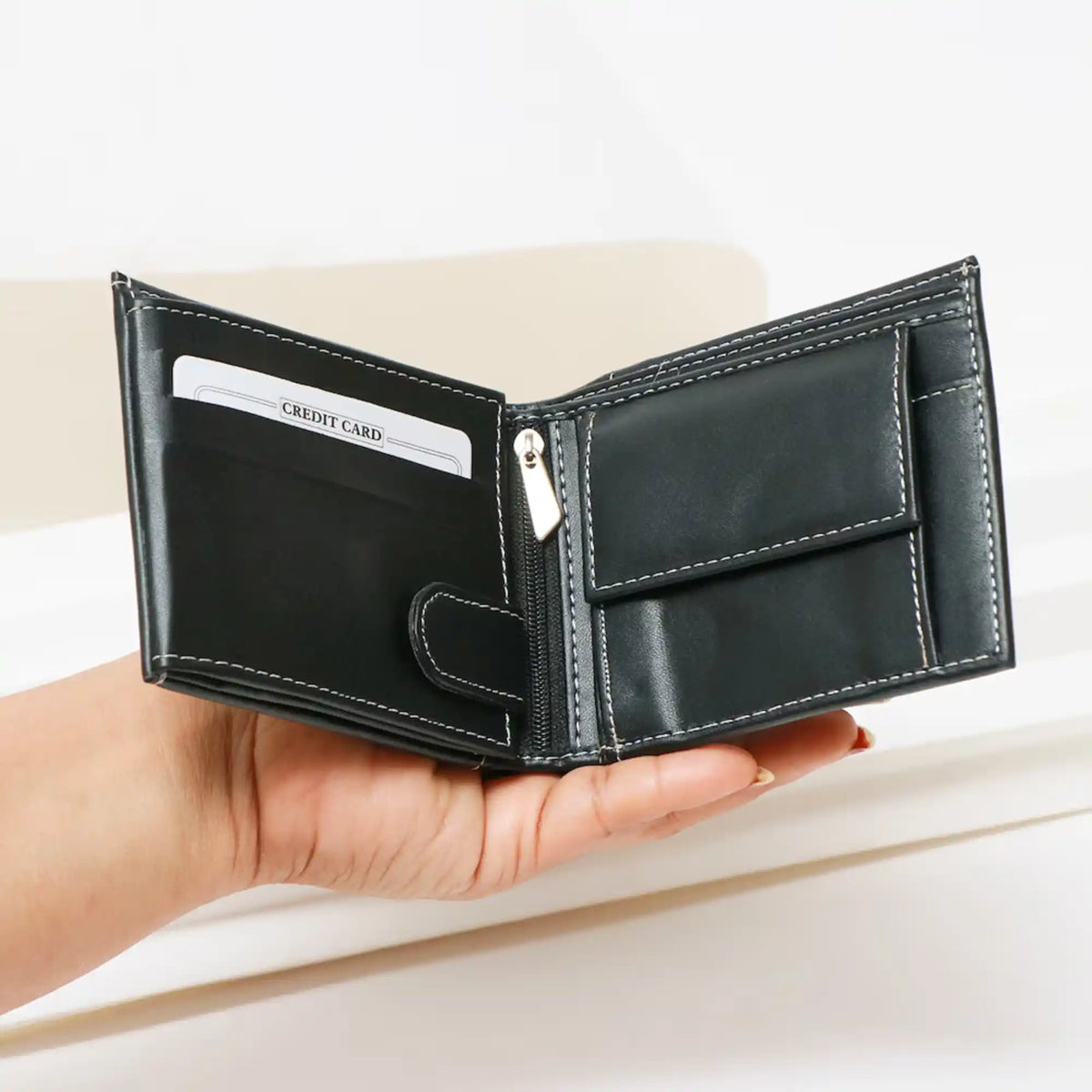 Hand holding black leather wallet with yellow stitching and card slots