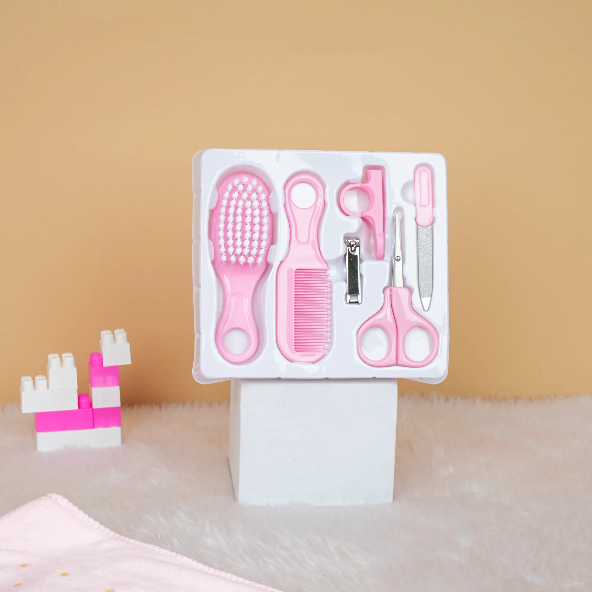 Set of pink grooming tools including a brush, comb, scissors, and clip in packaging on a beige surface.