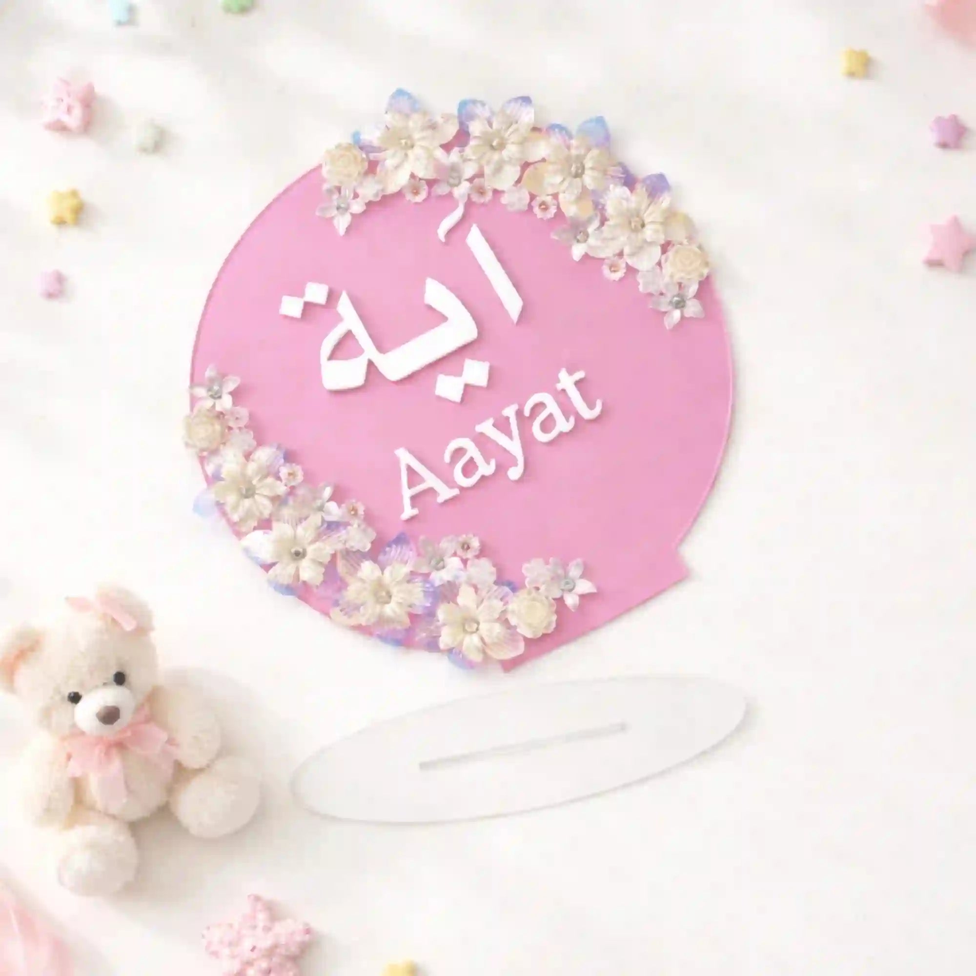 Kids Floral Pearl Name Frame with Stand in pink featuring name 'Aayat' in Arabic and English, adorned with white and purple flowers. Ideal for nursery décor. Main image