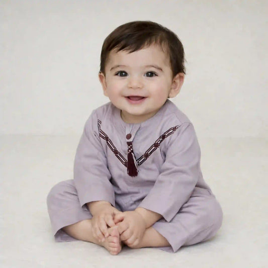 Smiling baby boy wearing a Purple Thobe Romper in soft Omani style, ideal for Ramadan and Eid celebrations. Perfect festive outfit from the Kids Collection.