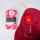 A red-themed Women's Namaz Essentials Hamper shown from above, including a rolled floral prayer dress, a red velvet prayer mat, a red mini velvet Quran box, matching red tasbeeh beads, and a digital counter.
