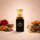 Luxurious Shanaya attar in a black and gold bottle, surrounded by raw fragrance ingredients including a red rose, smoking resin, spices, and honey.