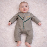 Close-up of baby boy in beige traditional outfit with embroidered details, lying on soft white surface