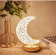 Decorative moon-shaped lamp on a table with a vase and book in the background