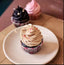 Cupcake with beige frosting on a white plate, with other cupcakes in the background.