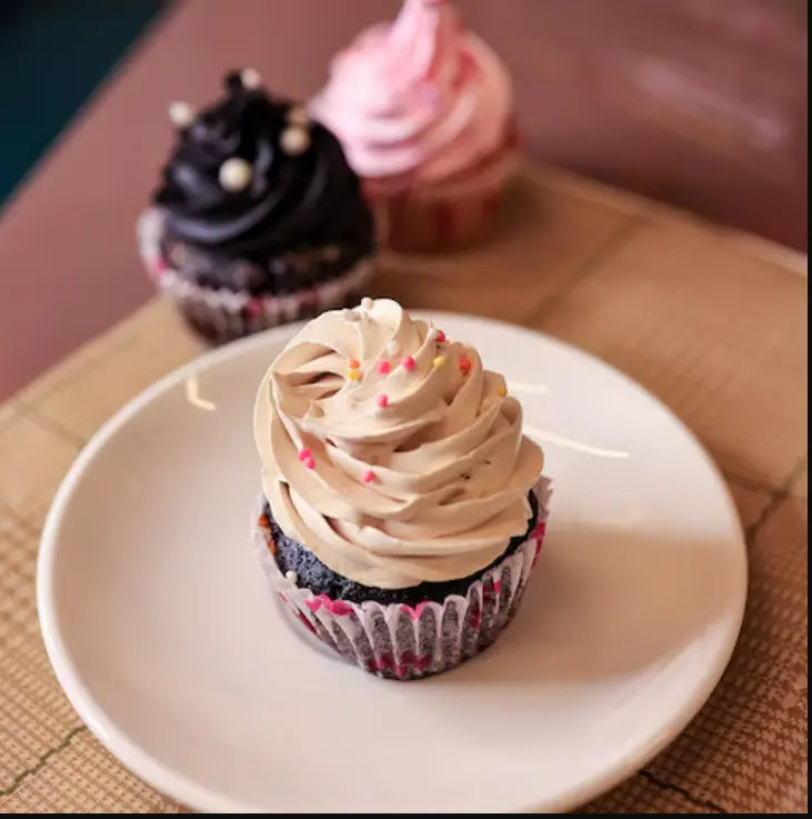 Cupcake with beige frosting on a white plate, with other cupcakes in the background. Main image