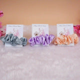 Set of three satin scrunchie bridal shower favors in grey, lavender, and peach with personalized cards, perfect for wedding gifts.