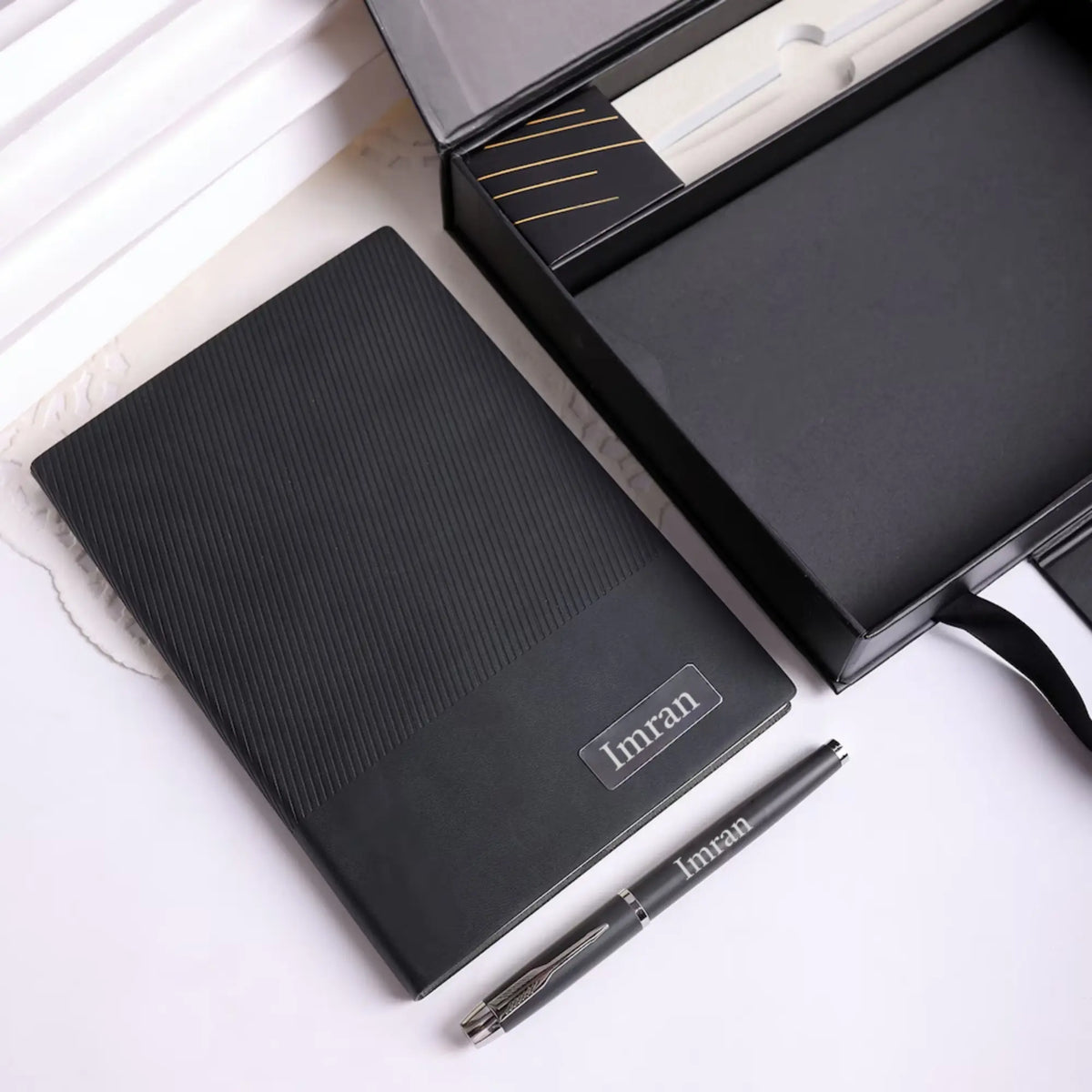 Black textured desk mat with a silver pen on white marble surface