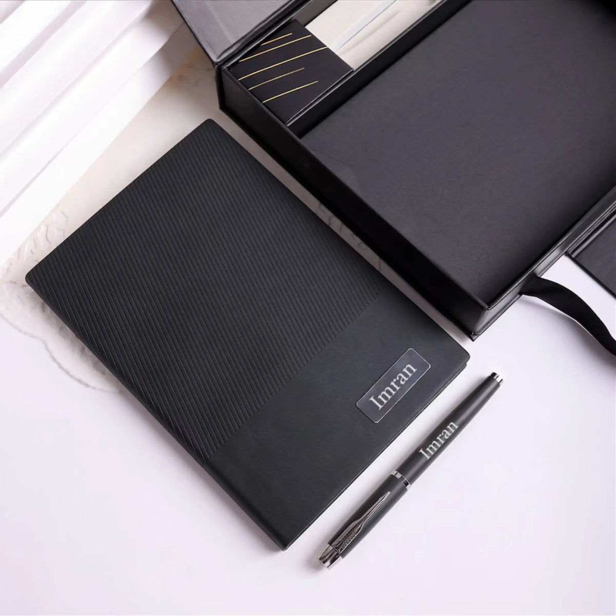 Black textured desk mat with a silver pen on white marble surface