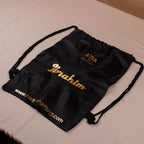 Black drawstring bag with gold text on a beige surface