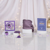 Front display of a purple Graceful Hijab Set on a reflective surface dotted with pearls and purple petals. The collection includes a rolled purple diamante hijab, a blue "Fortress of the Muslim" dua book, a framed purple digital tasbeeh, a purple beaded tasbeeh, and a matching tally counter, showcased against draped white curtains, warm fairy lights, and a traditional lantern.
