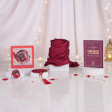 Front display of a red Graceful Hijab Set women's hamper on a reflective white surface with scattered pearls and red petals. The set includes a rolled dark red diamante hijab, a purple "Fortress of the Muslim" dua book, a red digital tasbeeh in a frame, a red beaded tasbeeh, and a red digital tally counter, set against a backdrop of white curtains, warm fairy lights, and a golden lantern.