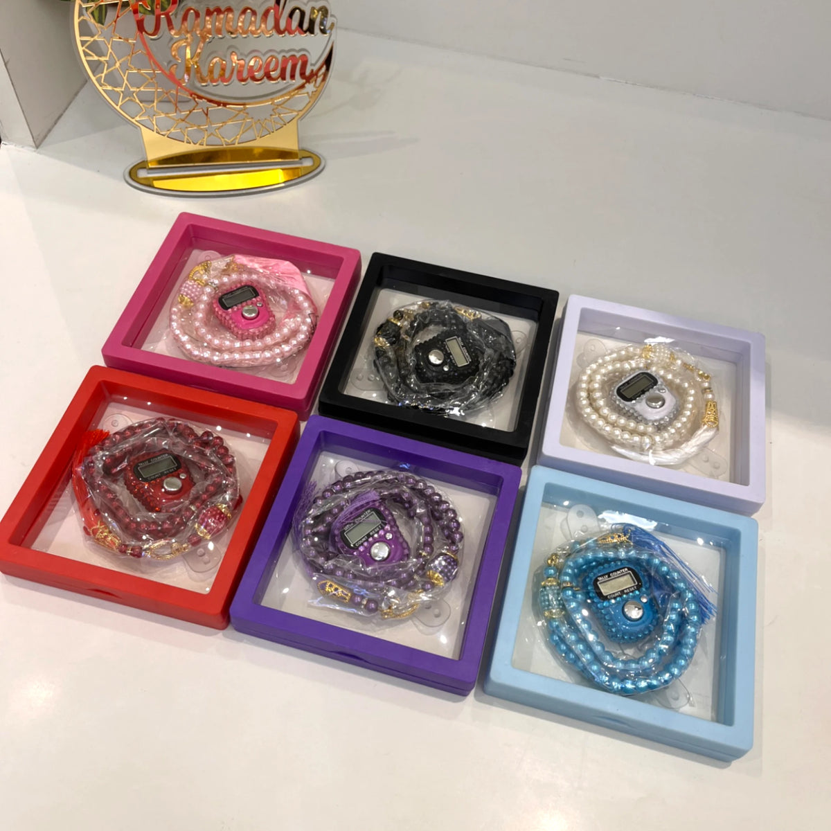 Colorful Transparent Tasbeeh Combos with digital counters in gift boxes, including red, pink, black, white, purple, and blue options for Islamic celebrations.