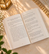 Open book on a white surface with other books stacked in the background