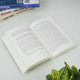 Open book on a white surface with other books stacked in the background