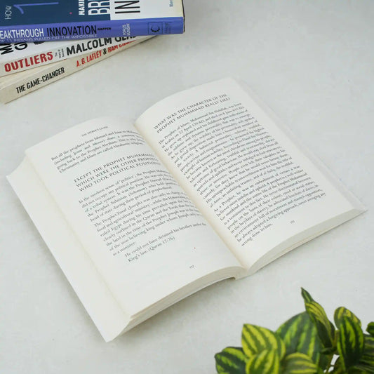 Open book on a white surface with other books stacked in the background