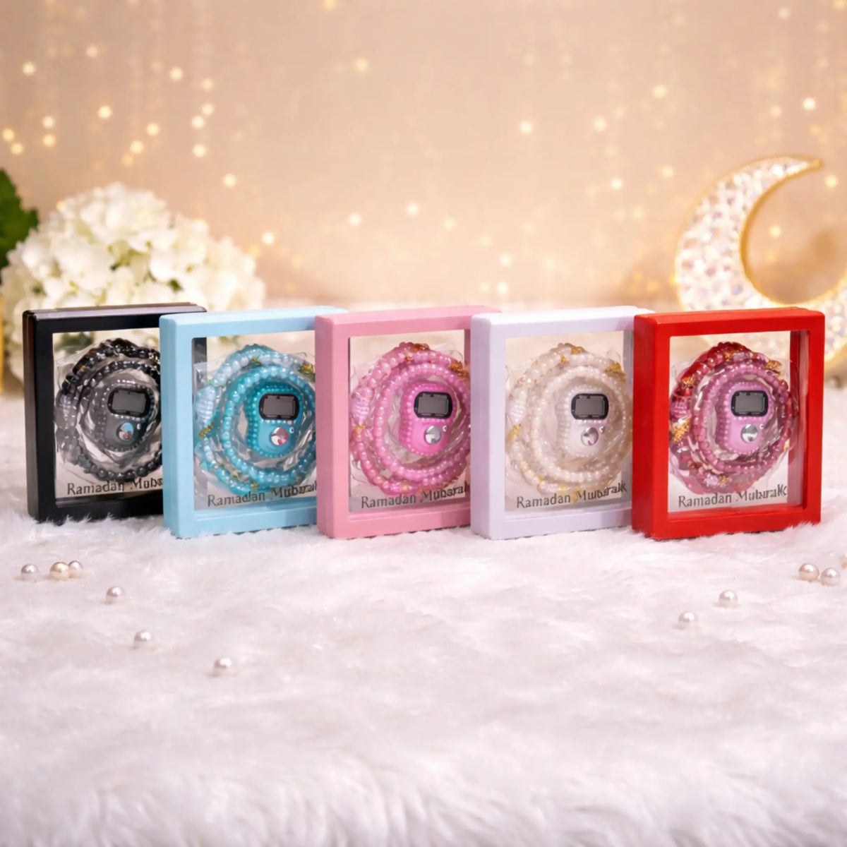 "Assortment of five Transparent Tasbeeh Combo Favors in black, light blue, pink, white, and red, displayed in clear PVC boxes featuring a Ramadan Mubarak insert."
