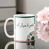 Umrah Mubarak Floral Mug with Arabic script and geometric floral design, 350 ml ceramic drinkware ideal for Umrah return gifts.