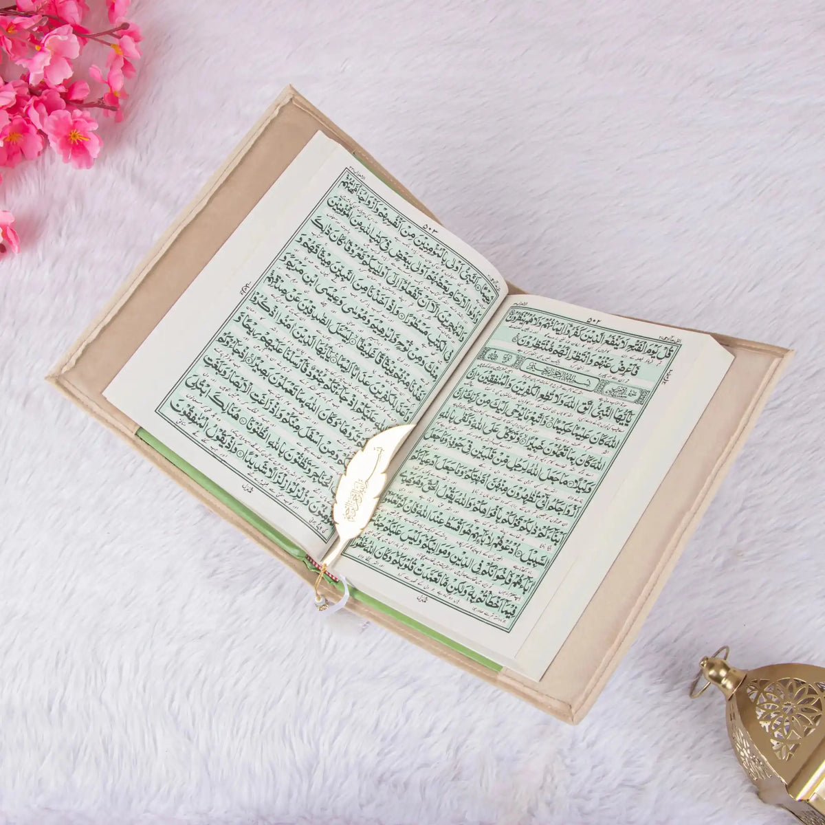 Open book with green text on a white surface with pink flowers
