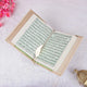Open book with green text on a white surface with pink flowers