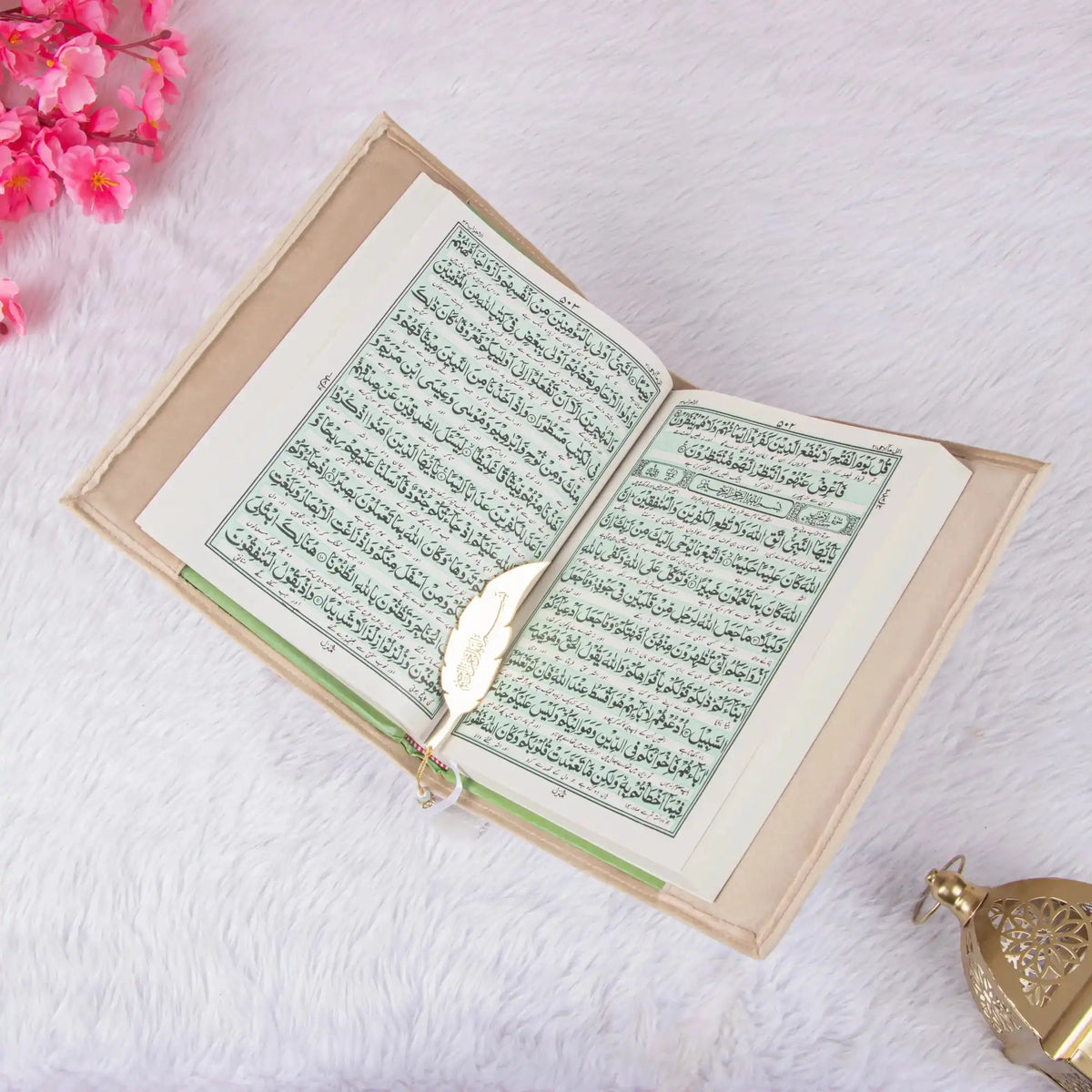 Open book with green text on a white surface with pink flowers