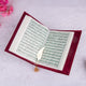 Open book with text, possibly a religious text, on a soft pink background with flowers.