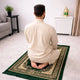 Man praying on green prayer rug wearing brown cap