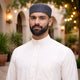 Man wearing white traditional attire with black prayer cap, outdoor setting for religious occasion