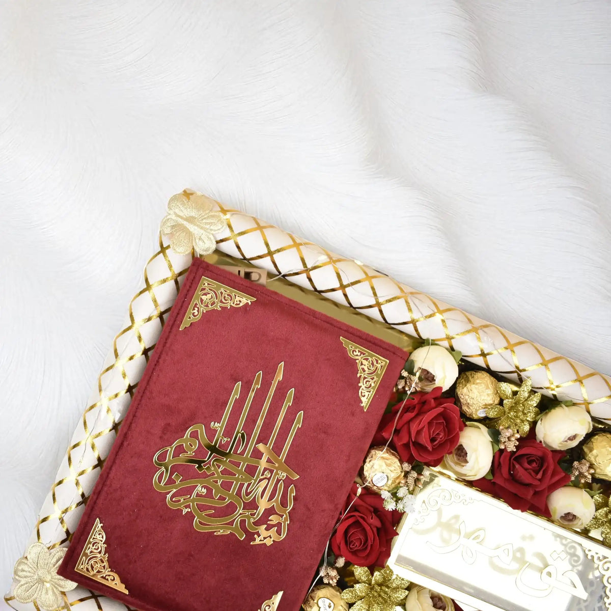Red book with gold design on a white surface with flowers and a box.